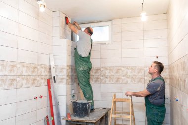 Orta yaşlı bir çalışan banyodaki duvara fayanslar döşemekle ilgilenir. Tecrübeli bir inşaat işçisi.