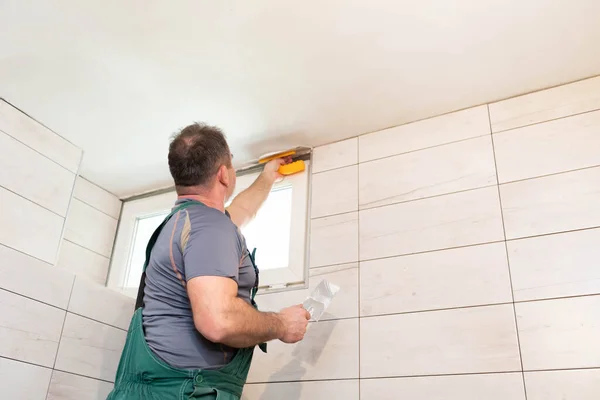 The worker applies plaster on the ceiling of the renovated bathroom. Construction worker in middle age. Green work clothes.