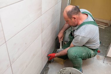 Bir inşaat işçisi dikkatlice jöleyi duvara yapıştırır. Profesyonel bir tiler seramik fayansı duvara yapıştırıcı ile basar..