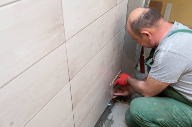 Bir inşaat işçisi dikkatlice jöleyi duvara yapıştırır. Profesyonel bir tiler seramik fayansı duvara yapıştırıcı ile basar..