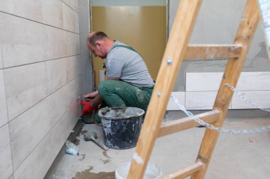 Bir inşaat işçisi dikkatlice jöleyi duvara yapıştırır. Profesyonel bir tiler seramik fayansı duvara yapıştırıcı ile basar..
