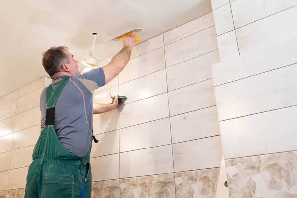 Un operaio edile applica un composto livellante al soffitto con una spatola in acciaio inossidabile. Lavori in altezza dal soffitto . — Foto Stock