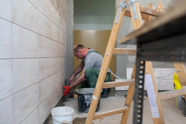 Un trabajador de la construcción pega cuidadosamente el esmalte a la pared. Un tiler profesional presiona la baldosa cerámica con adhesivo a la pared . — Foto de Stock