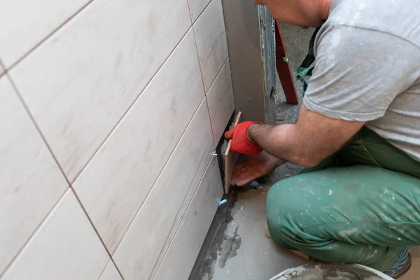 Un trabajador de la construcción pega cuidadosamente el esmalte a la pared. Un tiler profesional presiona la baldosa cerámica con adhesivo a la pared . — Foto de Stock