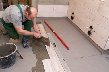 Genel inşaat işçisi. Seramik fayanslar için yapıştırıcı. İnşaatçı yere terracotta yapıştırıyor..