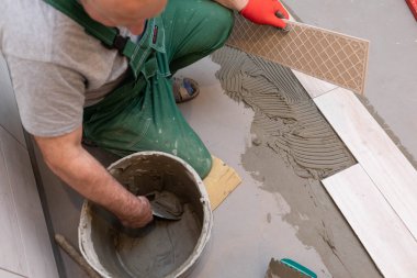 A construction worker lubricates the bottom of the ceramic tile with a metal trowel with special glue. clipart