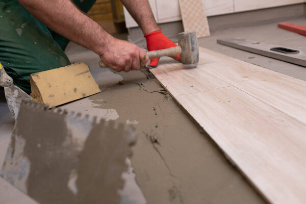 Rubber hammer. An experienced construction worker. Laying terracotta in the bathroom. Work clothes. He knocks with a hammer.