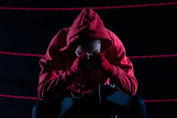 A lost fight of a strong MMA player. He is sitting in a chair. Right after losing the fight. Sad woman after a fight in the ring. In a hoodie.