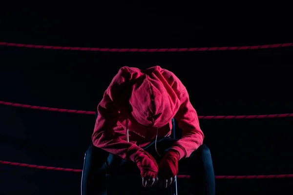 A lost fight of a strong MMA player. He is sitting in a chair. Right after losing the fight. Sad woman after a fight in the ring. In a hoodie.