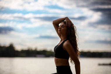 Bir kadın, dingin göl kenarında güzel bir yoga pozu veriyor. Huzur ve güç hissi veriyor.