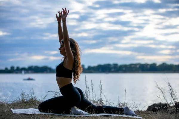 Bir kadın zarif bir şekilde yoga pozu veriyor. Sakin bir gölün yanında. Güzelliği ve huzuru kucaklıyor.