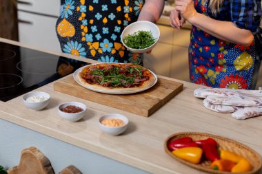 İnsanlar sıcak bir mutfakta taze yeşillikler ve canlı malzemelerle renkli bir yemek hazırlıyorlar.