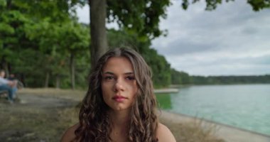 Düşünceli genç bir kadın sessizce sakin bir gölün kenarında oturur, tamamen doğanın güzelliğiyle çevrili.