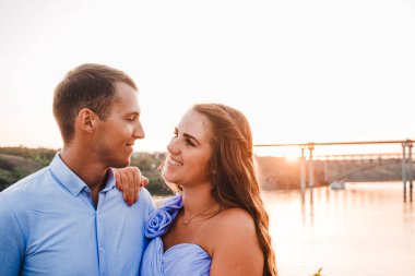 Aşık genç çift birbirlerine sarılır. Nehir kıyısında gün batımında iki aşık insan. Güzel bir kadın ve bir kayanın üzerinde duran adam. Beyaz bir çift. Nehirde Aşk Hikayesi