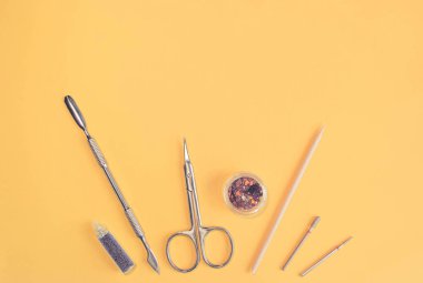 Sarı arka planda manikür ve pedikür aletlerinin üst görüntüsü. Güzellik moda konsepti. Demir ve Ağaç Kesicisi, Tırnak Makası, Mor Tırnak Parlatıcı, Değirmen Kesici Nozülleri. Boşluğu kopyala