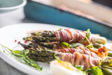 Taze kuşkonmaz pastırma roka domates ve yumurta ile beyaz bir plaka üzerinde sarılı.