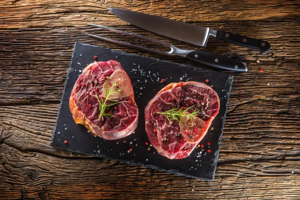 Two pieces raw beef shank on slate board and wooden table..
