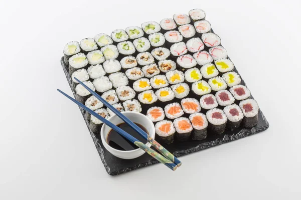 Suşi maki soya sosu ve üzerinde beyaz izole yemek çubukları ile kayrak gemide kümesi.