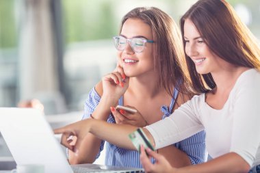 Bir kafede kredi kartı ve dizüstü bilgisayarı olan iki neşeli genç kadın bunları internetten rahatça satın alıyor..