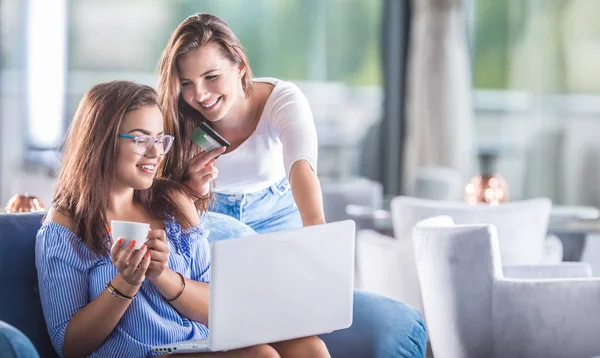 Bir kafede kredi kartı ve dizüstü bilgisayarı olan iki neşeli genç kadın bunları internetten rahatça satın alıyor..