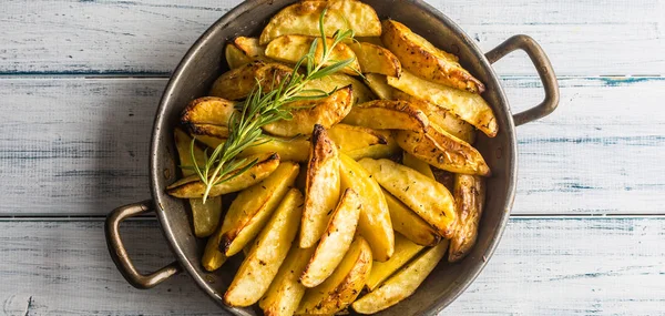 Roasted potatoes in a frying pan on wooden board.