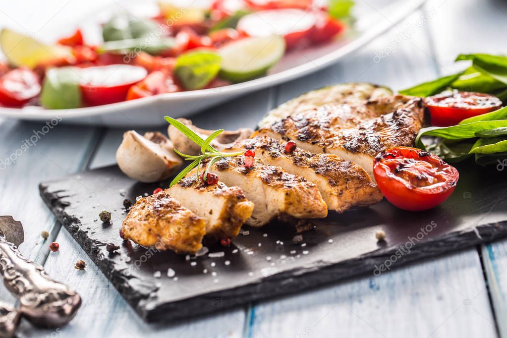 Grilled chicken breast on slate board herb spinach tomatoes and other vegetable.