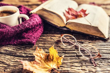 Fincan kahve eski kitap gözlük ve rustik ahşap masa üzerinde sonbahar yaprakları.