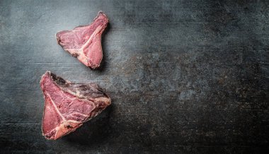 Yakın çekim ham T-bone biftek siyah kesme tahtası üzerinde.