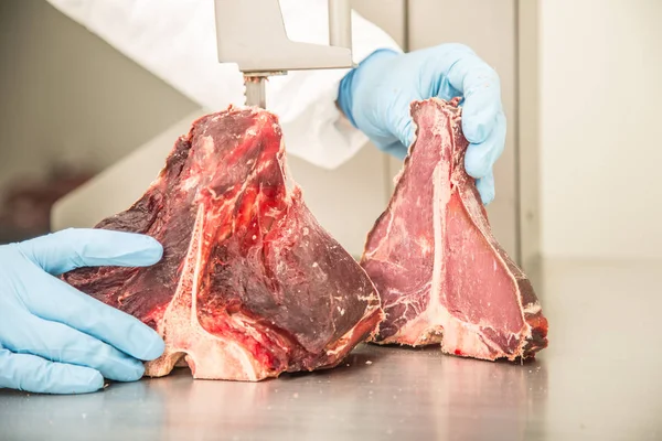 Worker on band saw cut meat in a meat shop. Slicing or cutting T-Bone steaks in market.