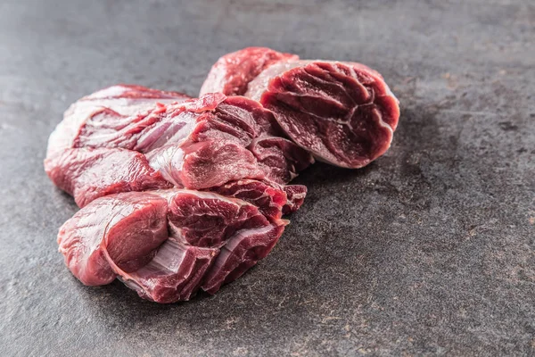Portion of raw beef shank on dark butcher board.