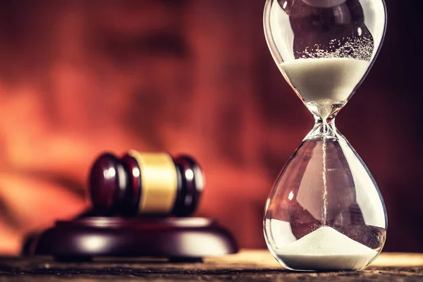 Modern hourglass in running time and justice hammer on wooden table.