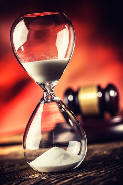 Modern hourglass in running time and justice hammer on wooden table.