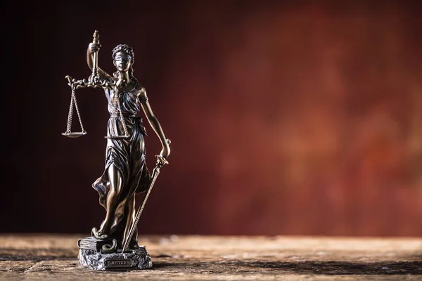 Lady Justicia holding sword and scale bronze figurine on wooden table.