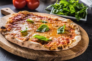 Geleneksel İtalyan pizza margarita fesleğen domates ve parmesan ile yuvarlak ahşap tahta üzerinde.