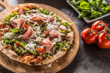 Prosciutto roka domates ve parmesan İtalyan pizza ahşap yuvarlak tahta üzerinde.