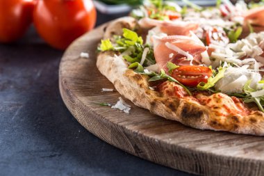 Prosciutto roka domates ve parmesan İtalyan pizza ahşap yuvarlak tahta üzerinde.
