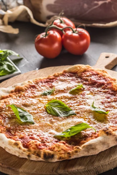Italian traditional pizza margarita on round wooden board with basil tomatoes and parmesan.