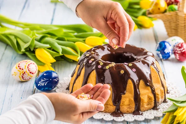 チョコレート艶出しとおいしい休日スロバキアとチェコ ケーキ Babovkaケーキを飾る女性の手 イースターの装飾 春のチューリップと卵 — ストック写真