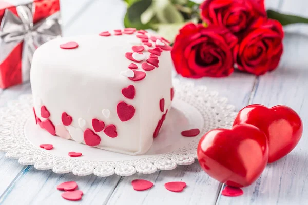 赤いハートのハートの形をしたマジパンの白いケーキ リボンからの贈り物は赤いバラの装飾花束 結婚式やバレンタインの日の概念 — ストック写真