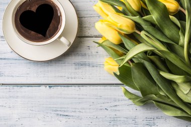 Ahşap masa üzerinde kalp ve bahar lale ile kahve görünümü Kupası formun üstü.