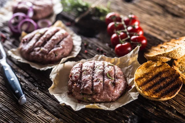 Raw burgers on wooden table with onion tomatoes herbs and spices.