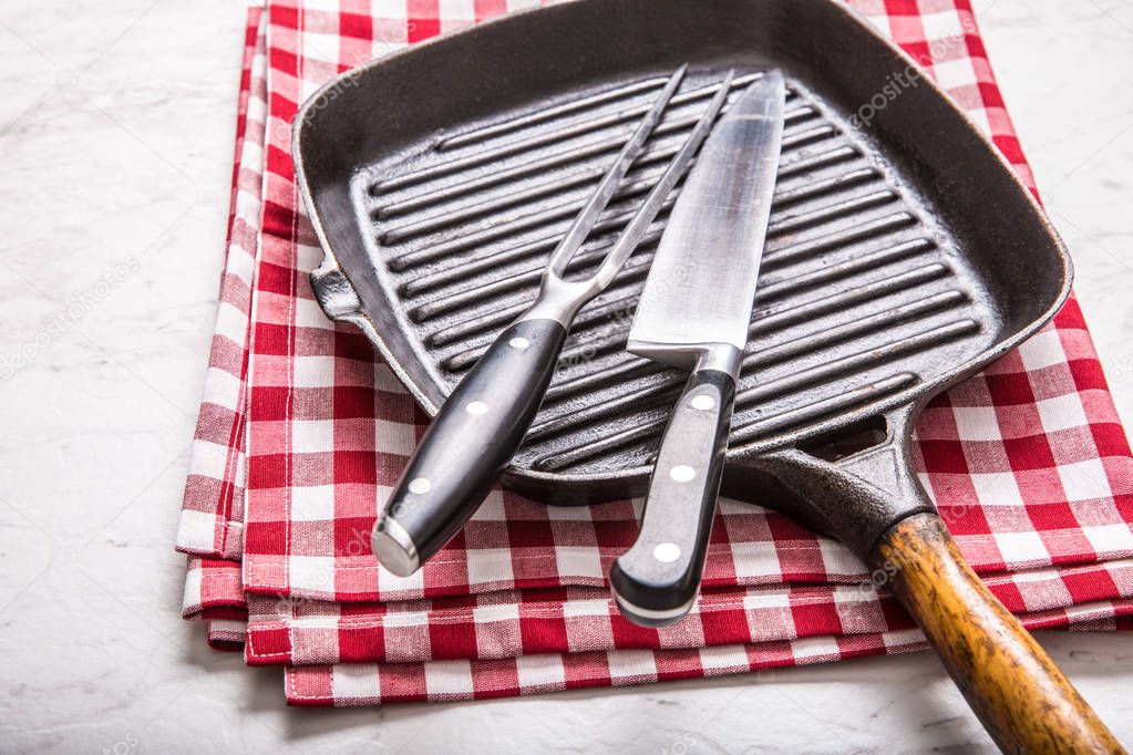 Empty grill pan on marble table with red tablecloth knife and fork.