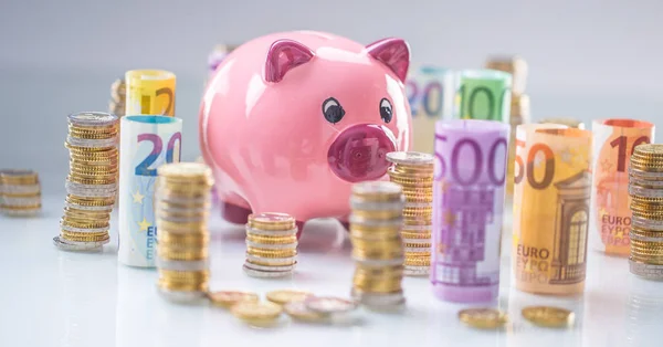 Pink piggy bank in the middle of rolled euro banknotes and tower — Stock Photo, Image