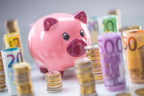 Hucha rosa en medio de billetes en euros laminados y torre — Foto de Stock