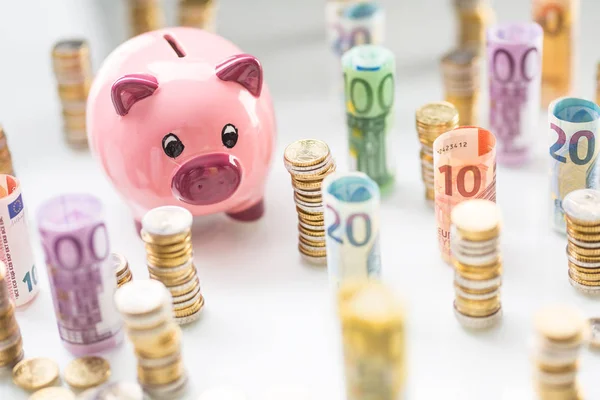 Rosafarbenes Sparschwein inmitten von gerollten Euro-Banknoten und Münztürmen — Stockfoto