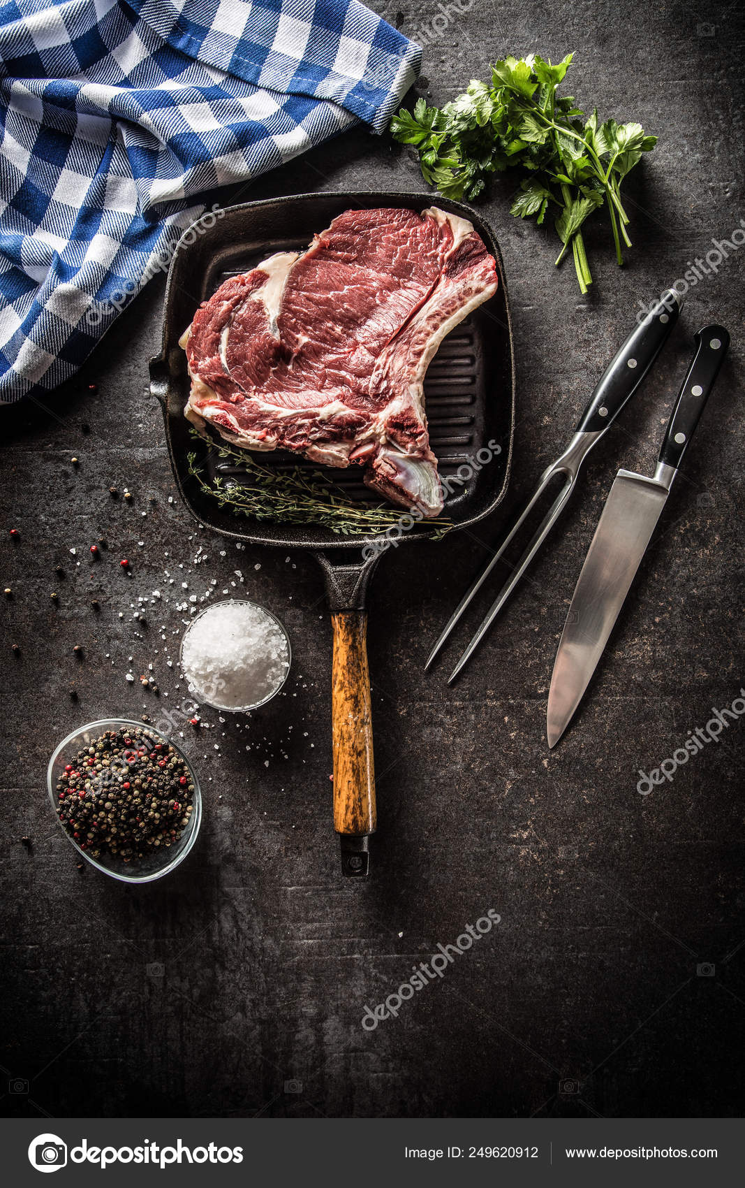 Rib eye steak in grill pan with herbs salt pepper fork and knife Stock
