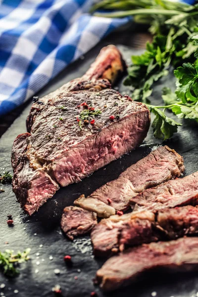 Carne de tomahawk recién asada en plato de pizarra con sal pimienta romero y hierbas de perejil. Trozos rebanados de jugoso bistec de res — Foto de Stock