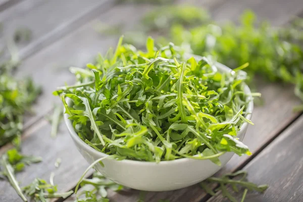 Fresh arugula salad in white dish on wooden table — Stock Photo, Image