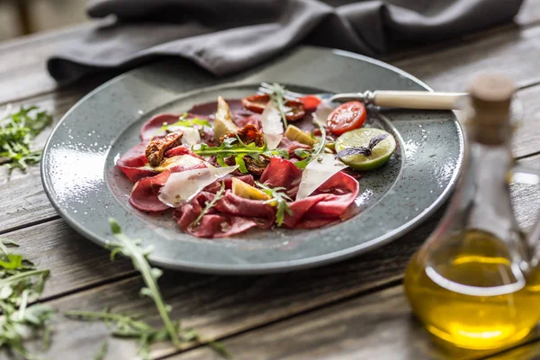 Beef carpaccio on plate with dried tomatoes artichokes arugula and parmesan cheese — Stock Photo, Image