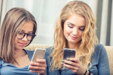 Oturma odasında akıllı telefonlar kullanarak iki genç girs veya kız kardeş